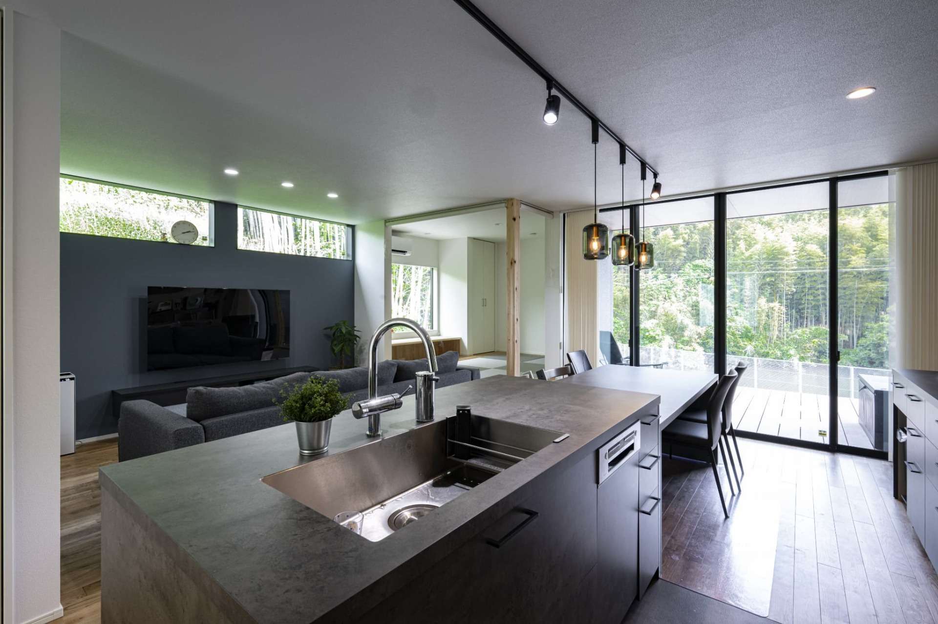 グレーのアイランドキッチンと木目調のダイニング。手元の作業スペースと、背面の造作棚へ家電を配置するための専用コンセントが、一級建築士による家事効率を最優先した高性能住宅の設計を象徴している。