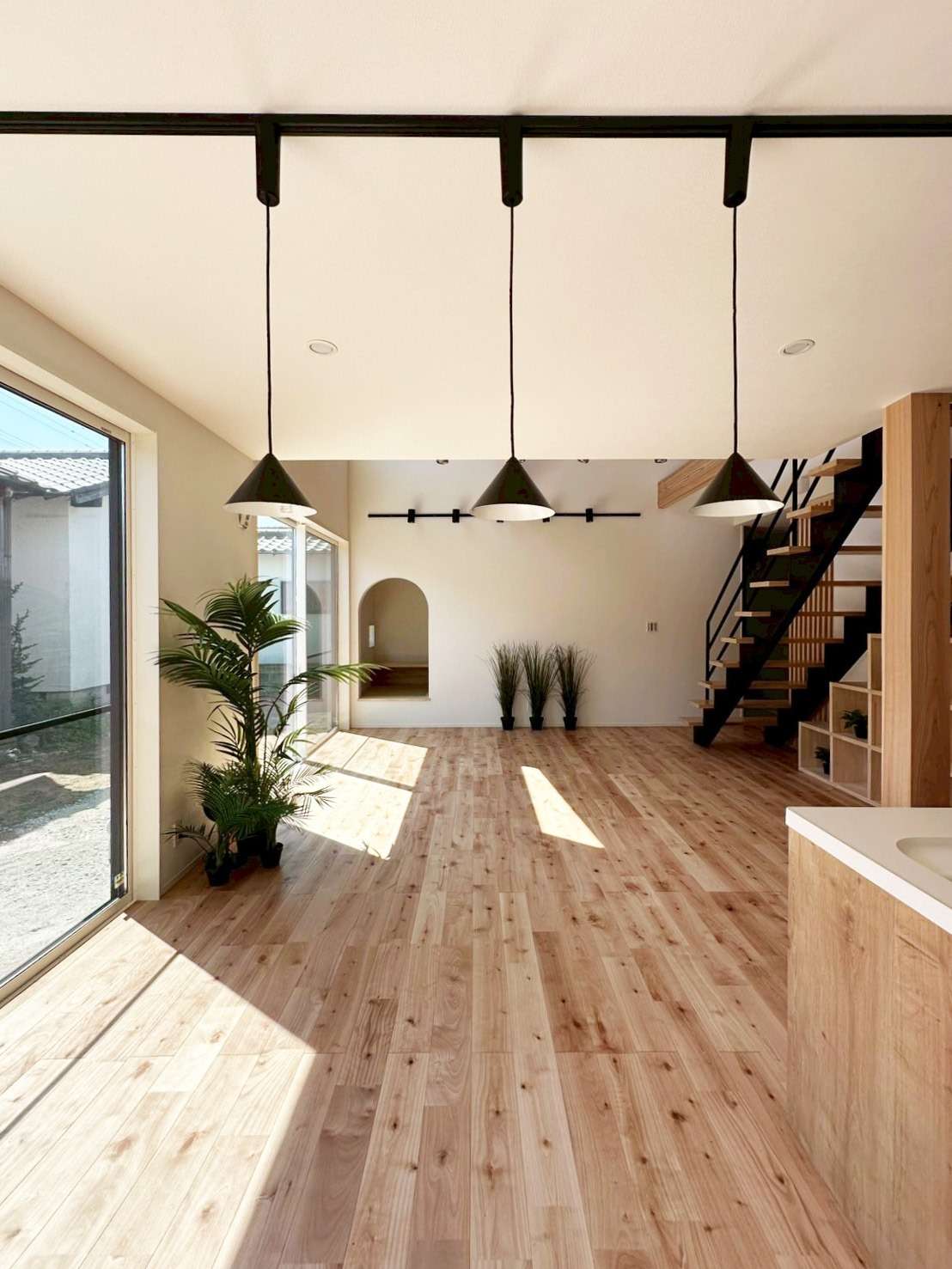 福津市で叶える「自然と共生する」住まい。無垢材の床が心地よい大空間のLIVING（リビング）。3連のペンダントライトとスケルトン階段がアクセントの、明るく開放感あふれる一級建築士設計の注文住宅内観。