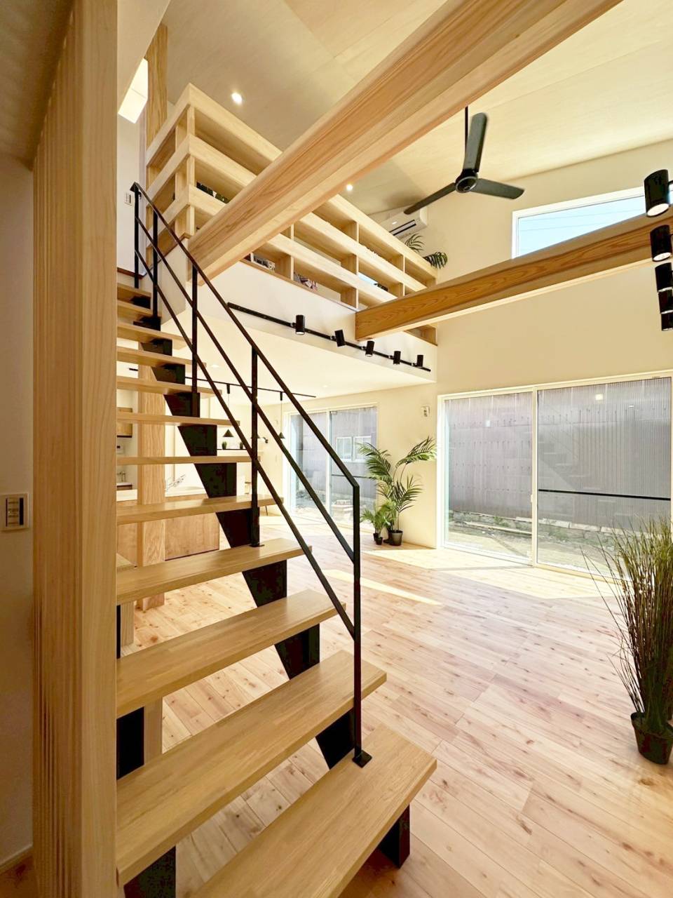 開放的な吹き抜けに設置されたブラックのシーリングファン。リビング階段と吹き抜けを利用して家全体の空気を循環させ、温度ムラをなくすZEH基準の高性能住宅設計。