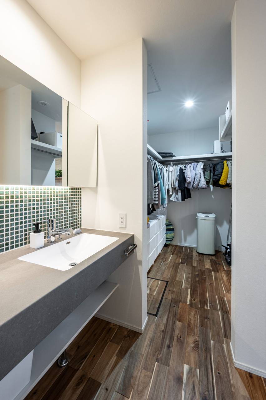 「洗う・干す・しまう」を最短距離で結ぶ、平屋ならではの洗面サンルーム動線。モザイクタイルがアクセントのスタイリッシュな造作洗面台と、大容量のファミリークローゼットが隣接する家事ラクな間取り。